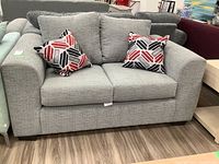 Front view of light gray fabric loveseat with two square throw cushions with geometric pattern in black, red, and white.