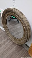Angled view of round wood frame mirror, showing carved detail and scratches on frame.