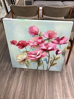 Full view of frameless floral canvas print showing pink and red flowers on a light background, leaned against chair on wood floor.