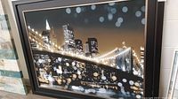 Front view of framed print showing the night skyline with a bridge and city buildings.