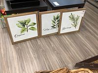Three framed herb motif prints (oregano, bay leaves, rosemary) displayed side by side on floor