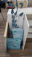 Photo showing blue metal leaf wall decor and two canvas prints with bird images resting against furniture