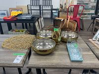 Photo of 3 gold-colored hammered metal bowls, a gold-colored geometric vase, a blue ceramic tray with 3 glass tea light holders, and a gold cordage doily. Items spread on a wooden table in a showroom.