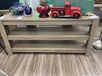 Front view of the wood finish media stand showing three open shelves and top surface with minimal wear.