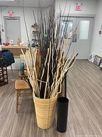 Full view of tall bamboo vase filled with long decorative branches and black metal vase beside it