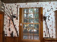 Overall view of tools leaning on fruit-print wallpapered wall: two hay pitchforks, pulleys, cranks and stove tools visible.