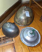 Three antique metal lids and one pewter bowl lid arranged on wooden floor showing size and condition.