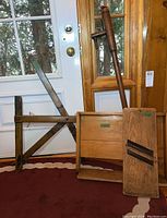 Overall view of the four wooden antique tools, including the water pump, slicer, kneading board, and crank lever support, positioned against a door.