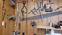Wall displaying antique tools including saws, pulleys, and iron hand tools arranged on wood paneling