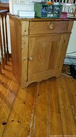 Front view of the wooden cabinet showing the drawer and door with round wooden knobs, natural wood finish, scratches visible