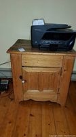 Front view of wood cabinet featuring one drawer and one door, with a white knob and a printer on top.