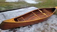 Full side profile of a wooden canoe on concrete surface with remnants of snow.
