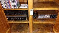 Wooden shelving unit holding a Zenith stereo receiver, Pioneer 2-disc CD player, cassette player, and various CDs on top shelf.