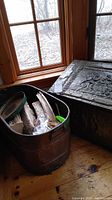 Photo of heavy metal tub filled with firewood and corner of embossed metal chest by window