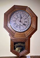 Octagonal wooden wall clock with upper clock face, Roman numerals and calendar days, 'Standard Time' pendulum visible through glass panel below.