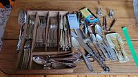 Full view of the wooden tray with assorted silver-tone cutlery including forks, knives, and spoons, plus extra cutlery and serving utensils alongside.