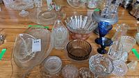 Various antique glassware items including bowls, cruet bottles, serving dishes, and small decorative glass pieces photographed on a wooden table.