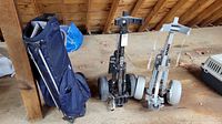 Side view of blue golf bag and two golf caddies, one black and one gray, on wooden floor in a loft space