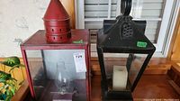 Two metal lanterns on a wooden surface, showing front view of both lanterns side by side