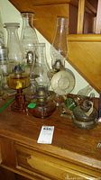 Multiple vintage oil lamps with clear and amber glass bases and tall chimneys arranged on a wooden surface.