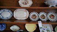Three shelves showing a collection of decorative and vintage plates including floral and fruit motifs