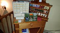 Wide view showing wooden thread rack loaded with spools of thread, white multi-drawer storage unit, green organizer with compartments, and assorted sewing tools on wooden desk.