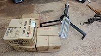 Full view of skeet shooter device with 4 boxes of clay targets stacked next to it on wooden floor.