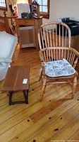 Photo of vintage wooden chair with spindle back and armrests, featuring a floral cushion on the seat, next to a small wooden folding table on a wooden floor.