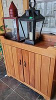 Front and side view of pine wood wash stand with vertical panel doors and metal handles. Black lanterns and red lantern on top not included.