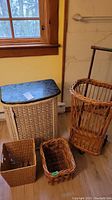 Photo of antique wicker cart, hamper, and two baskets placed on floor near window and wall.