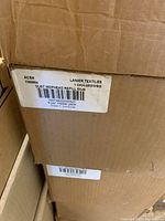 Close-up photo of a large cardboard box labeled with Lanier Textiles product code 1CHK-48WWBG, indicating dust mop head refill 5x48, 6 per master pack.