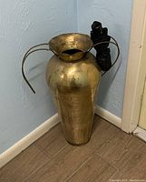 Front angle of the brass umbrella stand showing full height and detached side handle with black umbrella inside
