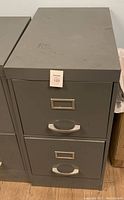 Front view of gray metal double drawer file cabinet with label holders and handles.