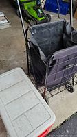 Photo showing black grocery buggy with metal frame and fabric bag next to a white topped cooler box.