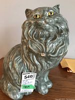 Front view of gray ceramic cat statue showing detailed fur texture, yellow eyes, and visible chip on chest fur area.