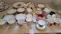 Wide view of a large assortment of china dishes, bowls, plates, tea cups, and mugs with varied colors and patterns, laid on a table.
