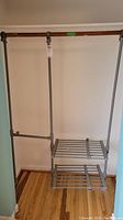 Front view of clip-on closet organizer hanging on wooden closet rod, showing two-tier metal shelves and vertical support rods.