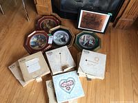 Overview of 13 collector plates; some in original boxes, four framed, and one framed copper engraving visible.