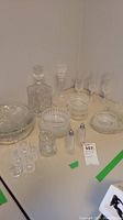 Photo of all glassware items showing decanters, bowls, plates, shakers, shot glasses, and tall glasses arranged on white surface.