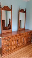 View of the dresser with six drawers and two attached mirrors with carved wood tops.