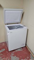 White Danby chest freezer with hinged lid open showing interior and wire basket. External temperature control knob visible.