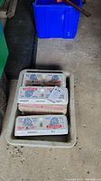 7 egg cartons stacked in a plastic bin, closed, showing labels with golf balls inside the cartons