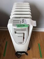 Front view of white DeLonghi oil-filled radiator heater with control panel and plugged-in power cord, including size label 14x7x26 inches.