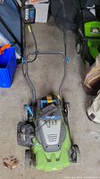 Green Craftsman 24 volt cordless lawn mower with push handle and battery mounted on top, blue battery compartment and black handle grips visible.