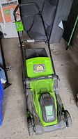 Greenworks electric lawn mower shown from above, depicting the battery compartment, handlebar and four wheels.