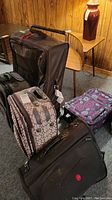 Photo of five pieces of luggage arranged on carpeted floor against wood panel wall with furniture in background.
