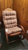 Wooden rocking chair with dark striped cushions on backrest and seat, set against a wood-paneled wall.