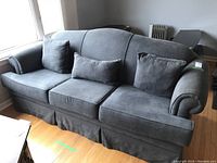 Front view of vintage dark gray fabric sofa with three matching throw pillows on hardwood floor near window.
