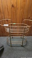 Front view of vintage brass and glass tea cart against wood-paneled wall showing top and bottom glass shelves