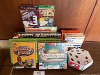 Photo showing multiple boxed adult games: Family Feud, Jeopardy Travel Edition, Reminiscing, Travel Wheel of Fortune, Schmuggler am Bord, Canadian History kits, and foam Yahtzee die.